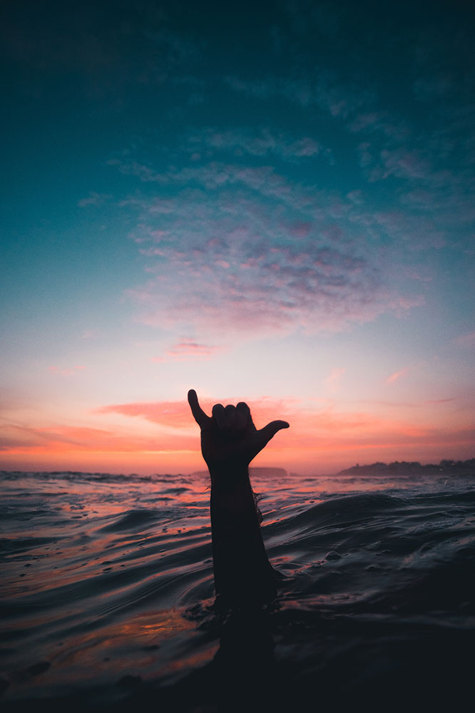 Arm sticking out of the water at sea, doing the shaka sign