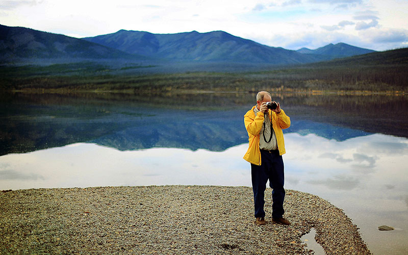 Man is yellow jacket taking photo of a lake