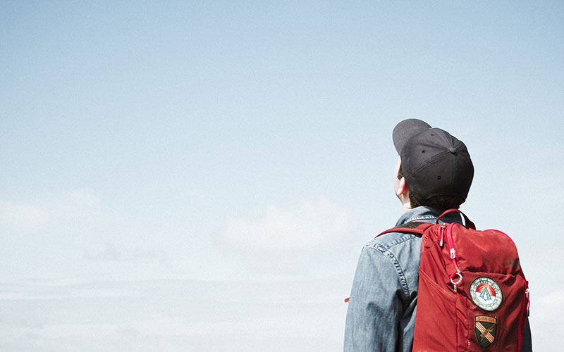 Boy with a cap and red bag on looking into the sky