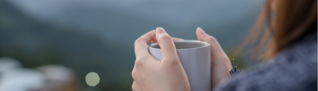 A woman holding a cup of coffee overlooking a green landscape