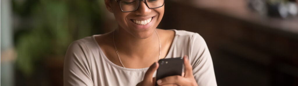 A woman smiling as she looks at her phone screen