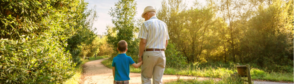 A grandfather and grandchild walking through a park.