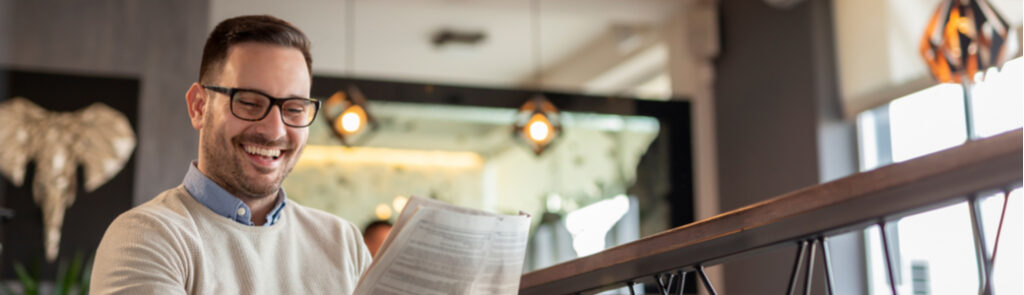 A man reading a newspaper while drinking coffee.