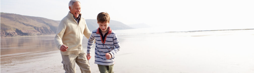 A grandfather and his grandson playing football on a beach.