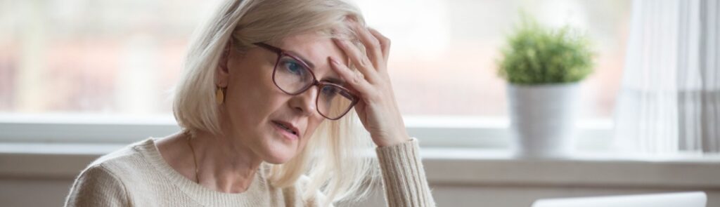 A retired woman looking worried while using a laptop.