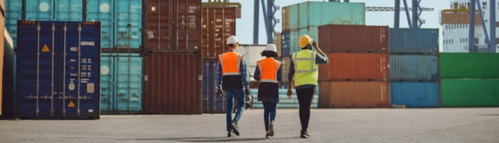 Workers walking through a shipping cargo container terminal depot.