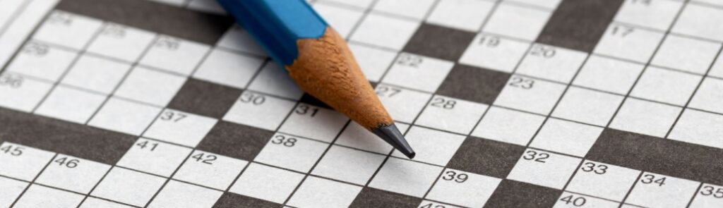 A close-up of an empty crossword puzzle with a pencil lying on top.
