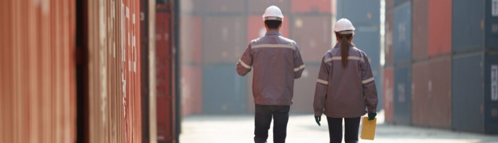 Two workers walking between shopping containers.