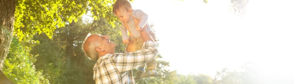 A grandfather playing with his young grandson in a park.