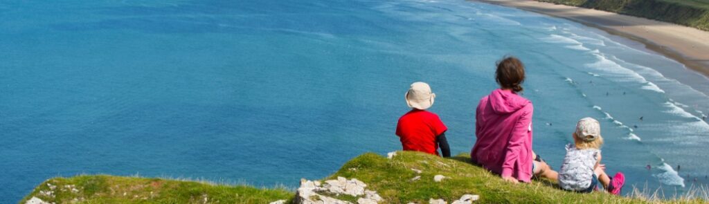 A family sitting on a clifftop overlooking a beach.