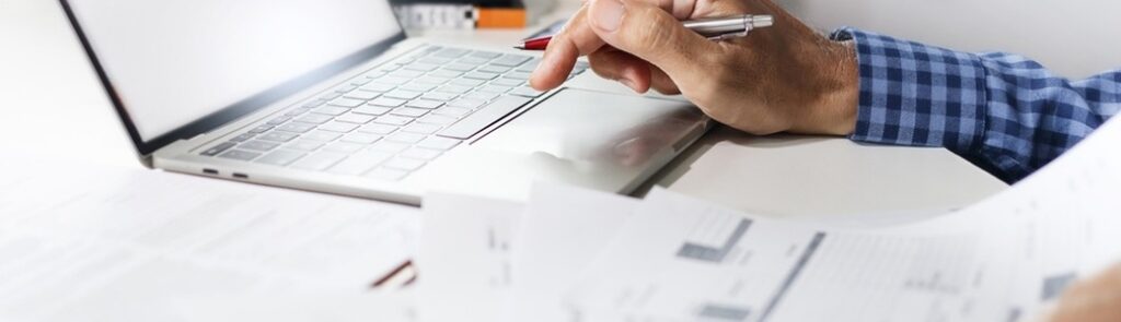 Man’s hands at a laptop, with financial paperwork