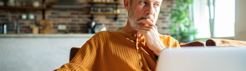 A man in his 50s thinking while using a laptop